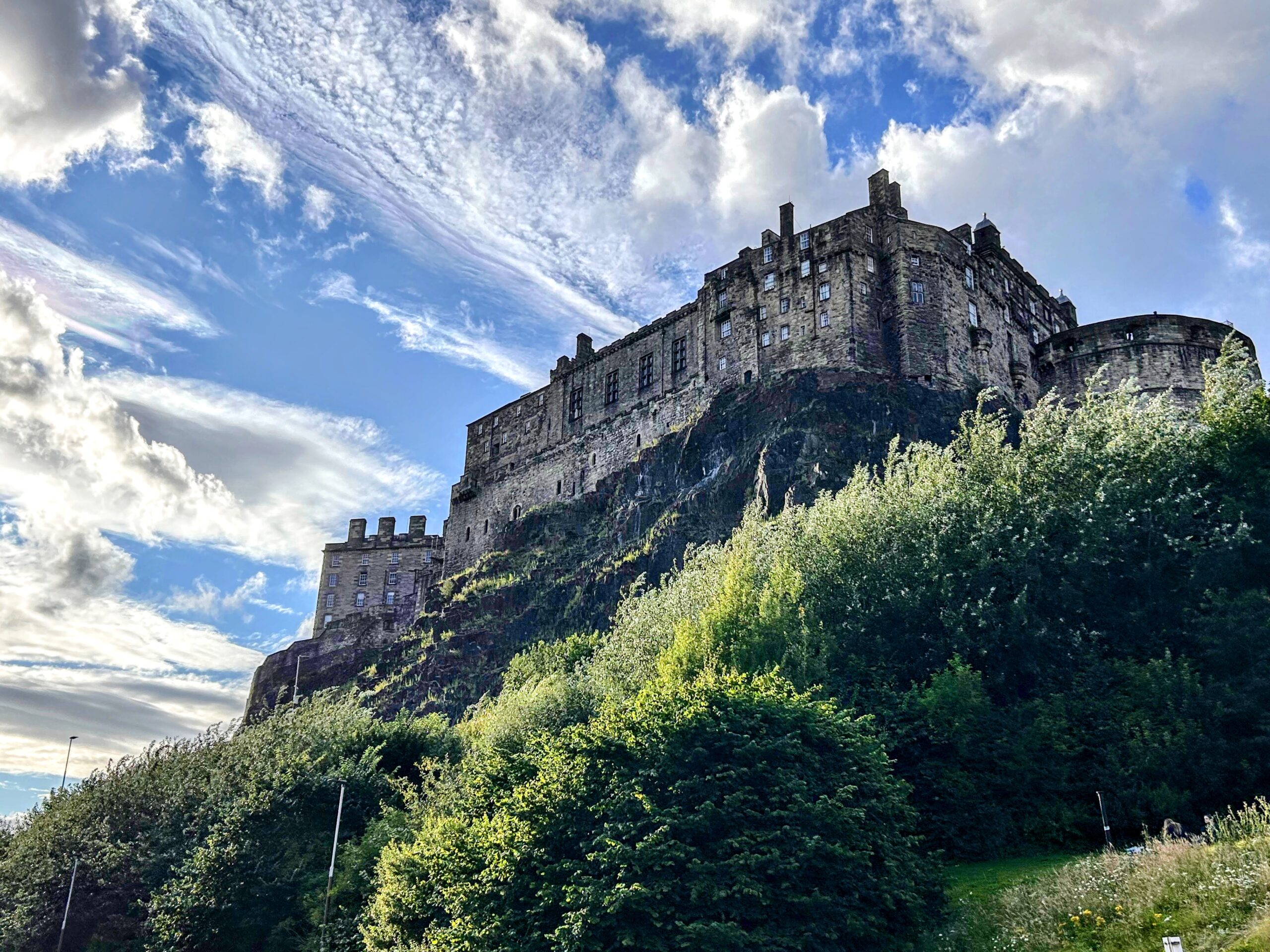A picture of a castle against a blue sky with clouds. There are green bushes in the foreground.